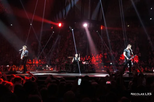 Concert de Muse : les musiciens sur scène sous des projecteurs rouges