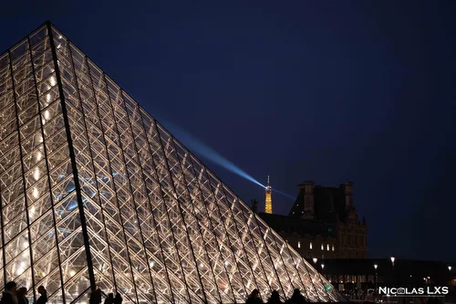 Pyramide du Louvre illuminée la nuit, avec le faisceau de la tour Eiffel